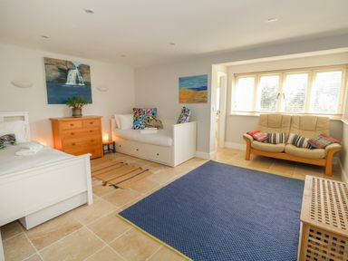 A room with two single beds a wooden chest of drawers a beige sofa with cushions and a blue rug on the floor at Sandy Combe in West Bay