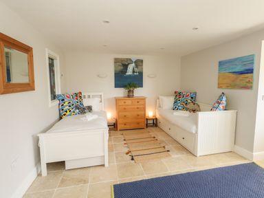 A bedroom with two white single beds a wooden chest of drawers and two colorful paintings on the walls at Sandy Combe in West Bay