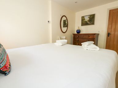A bedroom with a bed covered in white sheets and towels on it with a wooden dresser a chair an oval mirror and a painting on the wall at Sandy Combe in West Bay