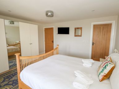 A bedroom with a wooden bed a pillow white towels a wardrobe with a mirror two wooden doors and a wall-mounted television at Sandy Combe in West Bay