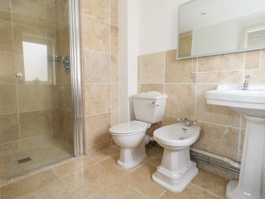 A bathroom with a shower, toilet, bidet, and sink with mirror at Sandy Combe in West Bay