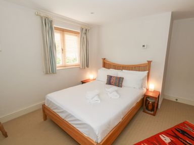 A bedroom with a wooden bed a colorful pillow white towels and two bedside tables with lamps at Sandy Combe in West Bay