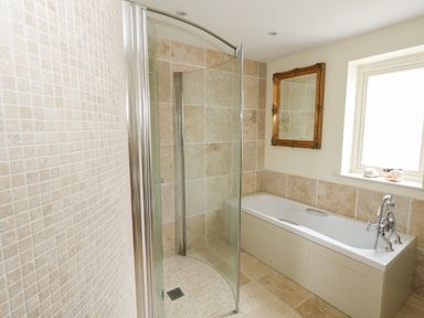 A bathroom with a curved glass shower screen a bathtub under a window and a mirror on the wall at Sandy Combe in West Bay