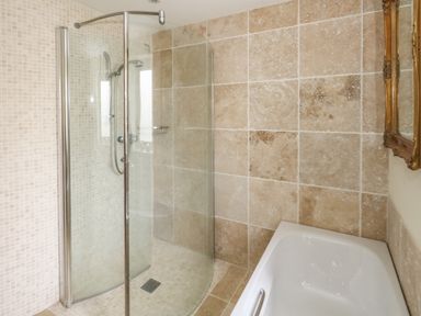 A bathroom with a glass shower enclosure and a white bathtub with tiled walls at Sandy Combe in West Bay