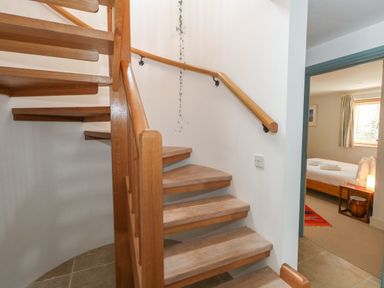 A wooden spiral staircase next to a doorway leading to a bedroom with a bed and window at Sandy Combe in West Bay