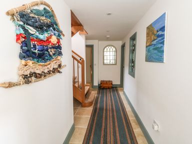 A hallway with a striped runner rug wooden stairs and wall decorations at Sandy Combe in West Bay