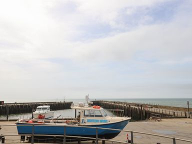 A boat named Hunters Moon docked near a pier with the sea and sky in the background at Sandy Combe in West Bay