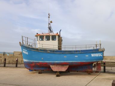 A blue and white fishing boat on land with registration WH856 at Sandy Combe in West Bay