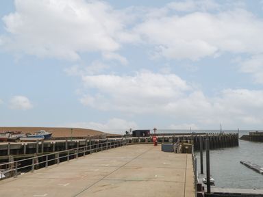 A concrete pier with boats on the left and water on the right under a cloudy sky at Sandy Combe in West Bay