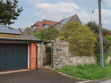 A stone wall with a wooden gate and a garage with solar panels on the roof at Sandycombe in West Bay