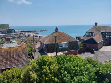 A view of houses with rooftops and greenery overlooking the sea at Sandy Combe in West Bay