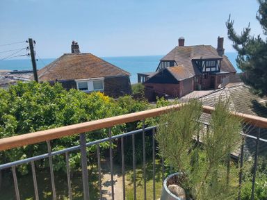 A view from a balcony with a railing overlooking houses trees and the sea at Sandy Combe in West Bay