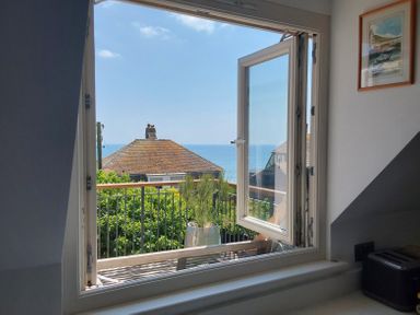 An open window overlooking rooftops sea and plants with a toaster on the countertop inside at Sandy Combe in West Bay