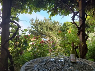 A garden view with a round metal table holding two glasses of wine and a wine bottle at Sandy Combe in West Bay