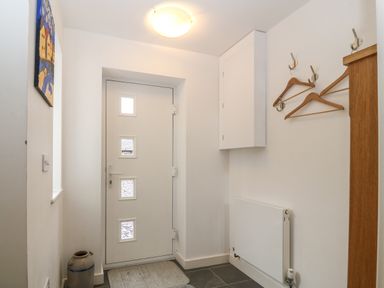 An entryway with a white door that has four small windows wooden coat hangers on hooks a radiator and a ceramic jug on the floor at Hen Gapel in Waunfawr Gwynedd
