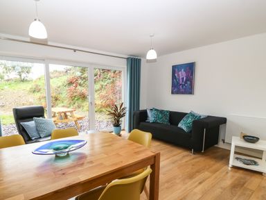 A dining table with yellow chairs and a living room with a black sofa and blue pillows at Hen Gapel in Waunfawr Gwynedd