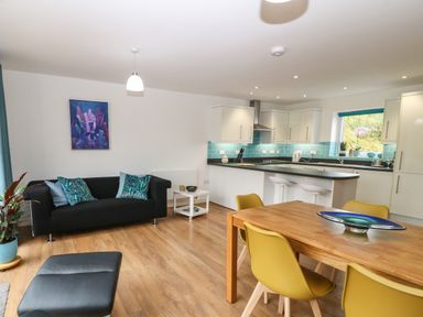 An open plan living room and kitchen with black sofa wooden dining table and yellow chairs at Hen Gapel in Waunfawr Gwynedd