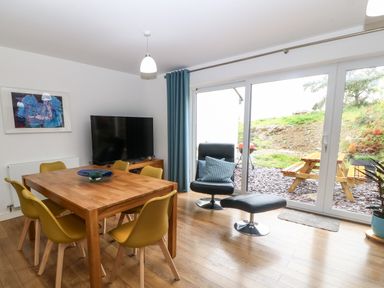 A dining area with a wooden table and yellow chairs next to a black chair and ottoman by sliding glass doors at Hen Gapel in Waunfawr Gwynedd