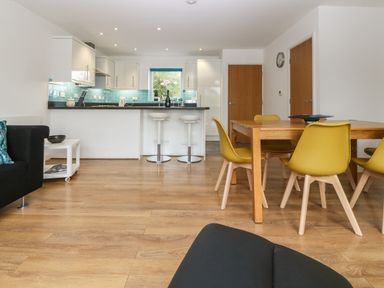 A kitchen and dining area with wooden floor yellow chairs and a counter with white bar stools at Hen Gapel in Waunfawr Gwynedd