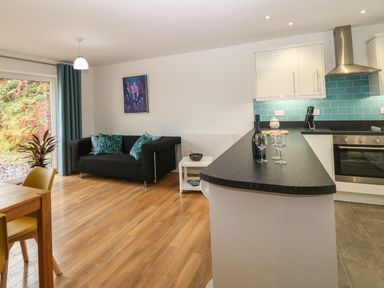 An open plan kitchen and living area with a black sofa and dining table at Hen Gapel in Waunfawr Gwynedd
