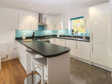 A kitchen with white cabinets black countertops turquoise backsplash and two white bar stools at Hen Gapel in Waunfawr Gwynedd