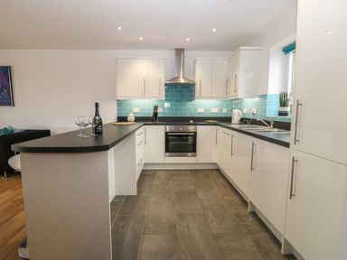 A kitchen with white cabinets black countertops and blue tile backsplash at Hen Gapel in Waunfawr Gwynedd
