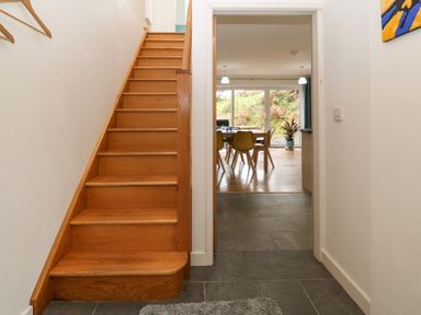 A wooden staircase next to a corridor leading to a dining area with chairs and a plant at Hen Gapel in Waunfawr Gwynedd
