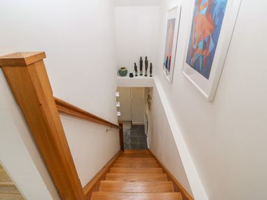 A wooden staircase with handrail leading down to a tiled floor with wall decorations at Hen Gapel in Waunfawr Gwynedd