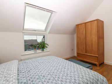 A bedroom with a bed covered in a patterned duvet two potted plants on a windowsill and a wooden wardrobe at Hen Gapel in Waunfawr Gwynedd