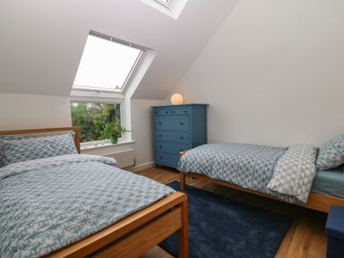 A bedroom with two single beds a blue chest of drawers a plant by the window and a dark rug on the floor at Hen Gapel in Waunfawr Gwynedd