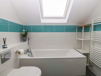 A bathroom with a bathtub under a skylight window a toilet a white shelf unit a towel radiator and a plant in a blue pot at Hen Gapel in Waunfawr Gwynedd