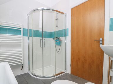 A bathroom with a corner shower enclosure a wooden door a white towel radiator and a sink at Hen Gapel in Waunfawr Gwynedd