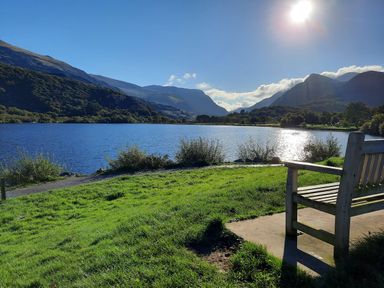 A wooden bench on grass near a lake with mountains in the background at Hen Gapel in Waunfawr Gwynedd