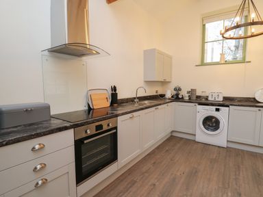 A kitchen with oven, washing machine, countertop appliances, and a window at Cwrt y Wennol in Salem near Clydach