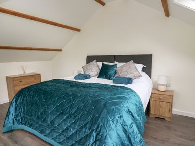 A bedroom with a bed with a teal quilt and pillows between two wooden bedside tables at Cwrt y Wennol Salem near Clydach
