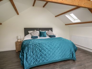 A bedroom with a double bed covered with teal bedding two wooden bedside tables with lamps and a skylight window at Cwrt y Wennol Salem near Clydach