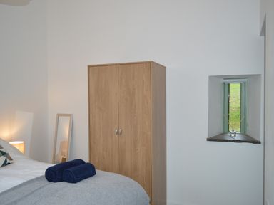 A bedroom with a wooden wardrobe a small window and towels on a bed at Cwrt y Wennol in Salem near Clydach
