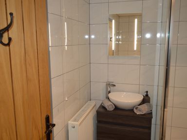 A bathroom with a round basin on a wooden cabinet two towels and a soap dispenser a mirror and a radiator at Cwrt y Wennol in Salem near Clydach