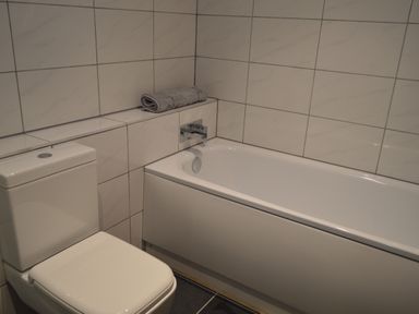 A bathroom with a toilet and a bathtub with a folded towel on the tiled ledge at Cwrt y Wennol in Salem near Clydach