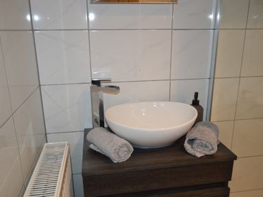 A bathroom sink with a modern faucet two rolled towels and a soap dispenser on a dark wooden cabinet at Cwrt y Wennol Salem near Clydach