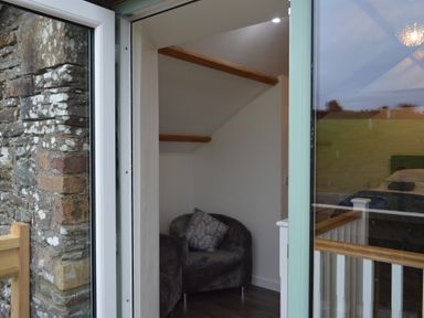 A small seating area with a dark armchair and pillow next to a staircase inside a building at Cwrt y Wennol in Salem near Clydach