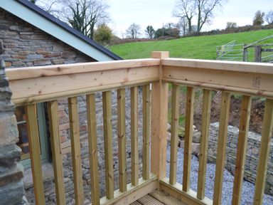 A wooden balcony railing outside a stone building with grass and trees in the background at Cwrt y Wennol in Salem near Clydach