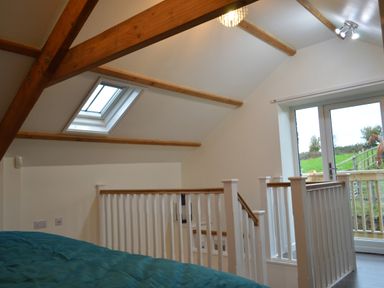 A bedroom loft with wooden beams skylight window white railing and glass door leading outside at Cwrt y Wennol Salem near Clydach