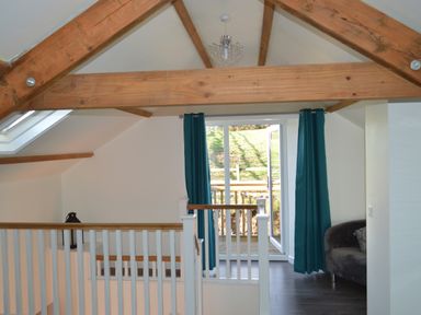A stairway landing with wooden beams blue curtains and a sliding door opening to a balcony at Cwrt y Wennol in Salem near Clydach
