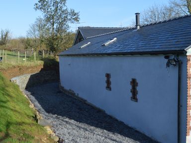 Exterior side view of a building with a tiled roof two small windows gravel path and green grass near Cwrt y Wennol in Salem near Clydach
