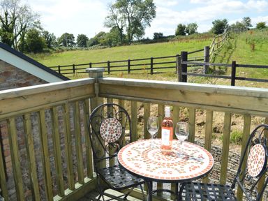 A small outdoor patio with a mosaic table holding a bottle of rose wine and two wine glasses with two metal chairs and a grassy field with a wooden fence in the background at Cwrt y Wennol in Salem near Clydach