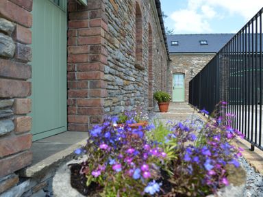 A stone building exterior with green doors a stone pathway potted plants and a black metal fence at Cwrt y Wennol Salem near Clydach