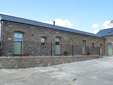 A stone building with green doors and windows and black metal railing outside at Cwrt y Wennol in Salem near Clydach
