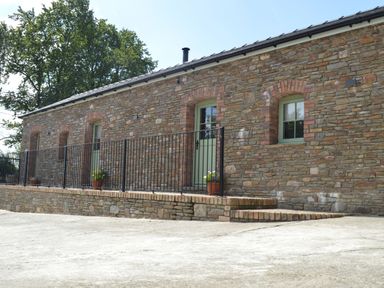 An exterior view of a stone building with green doors and windows a black metal railing and potted plants on the ledge at Cwrt y Wennol in Salem near Clydach
