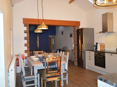 A kitchen and dining area with a table set for four with dishes glassware and chairs next to a stove and refrigerator at Cwrt y Wennol Salem near Clydach